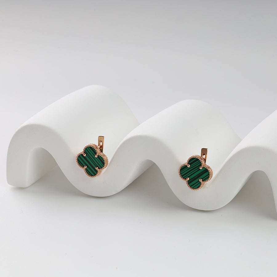 Pair of gold and green malachite clover earrings displayed on a white wavy stand, gemstone drop earrings.