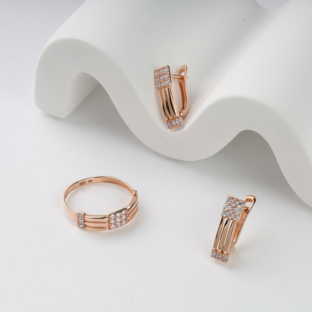 Rose gold jewelry set with cubic zirconia, including one ring and two huggie earrings on white display.