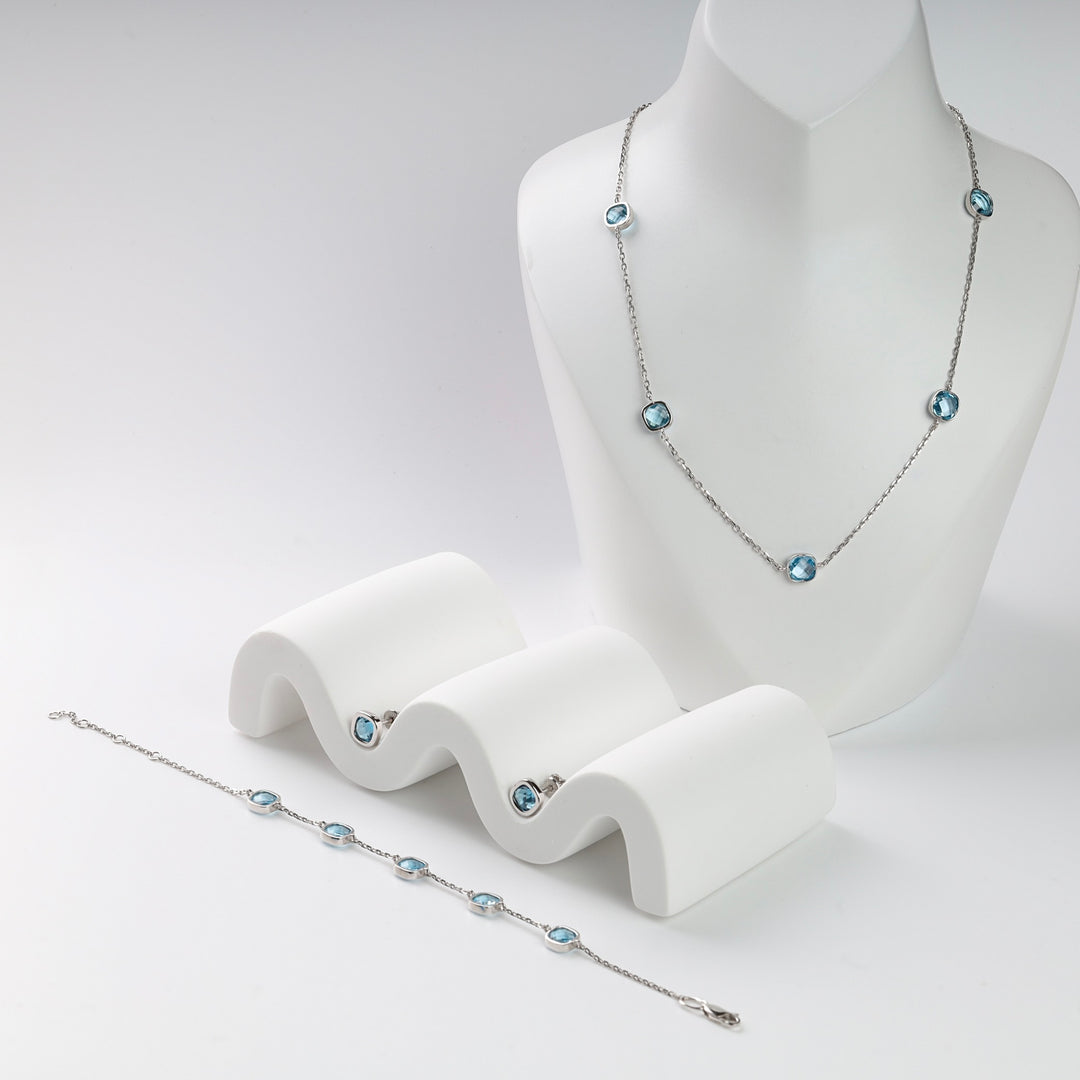 Silver necklace and bracelet set with round blue gemstones displayed on white holders.