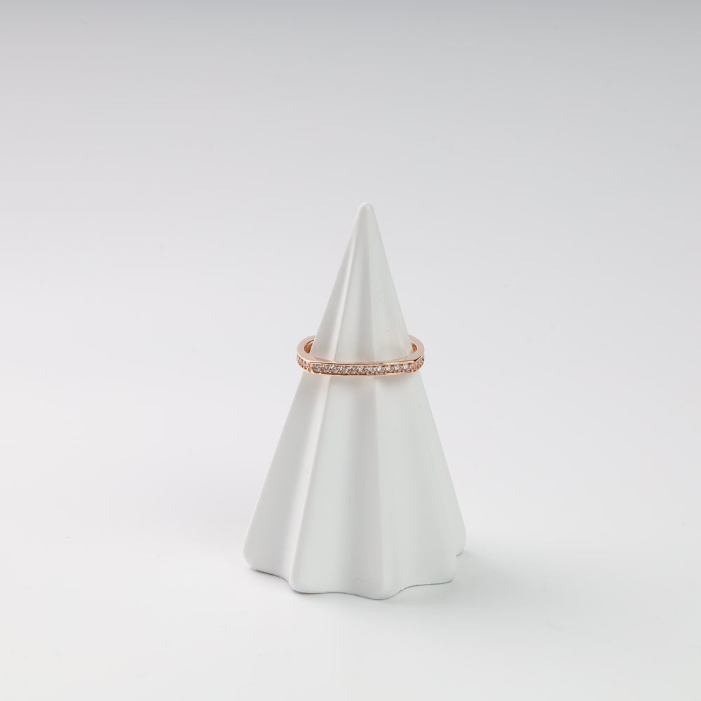 Rose gold ring with clear gemstones on a white cone display.