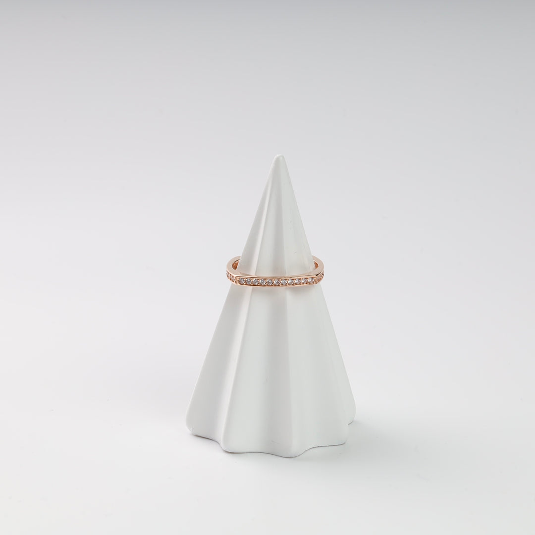 Rose gold ring with clear gemstones on a white cone display.