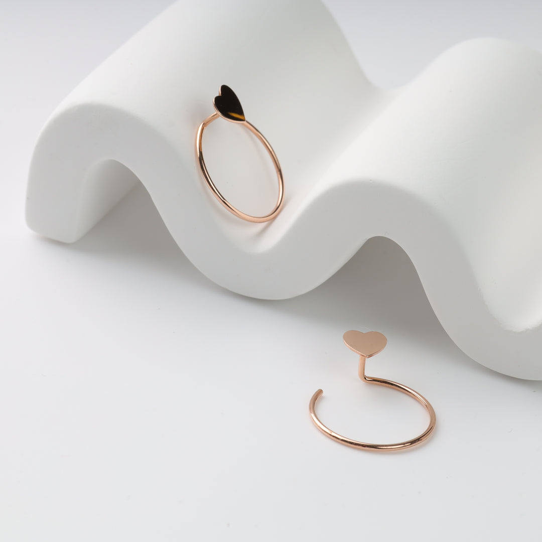 Two rose gold open heart rings, one with a black enamel heart, displayed on a white wavy stand as a rose gold heart ring and open ring pair.