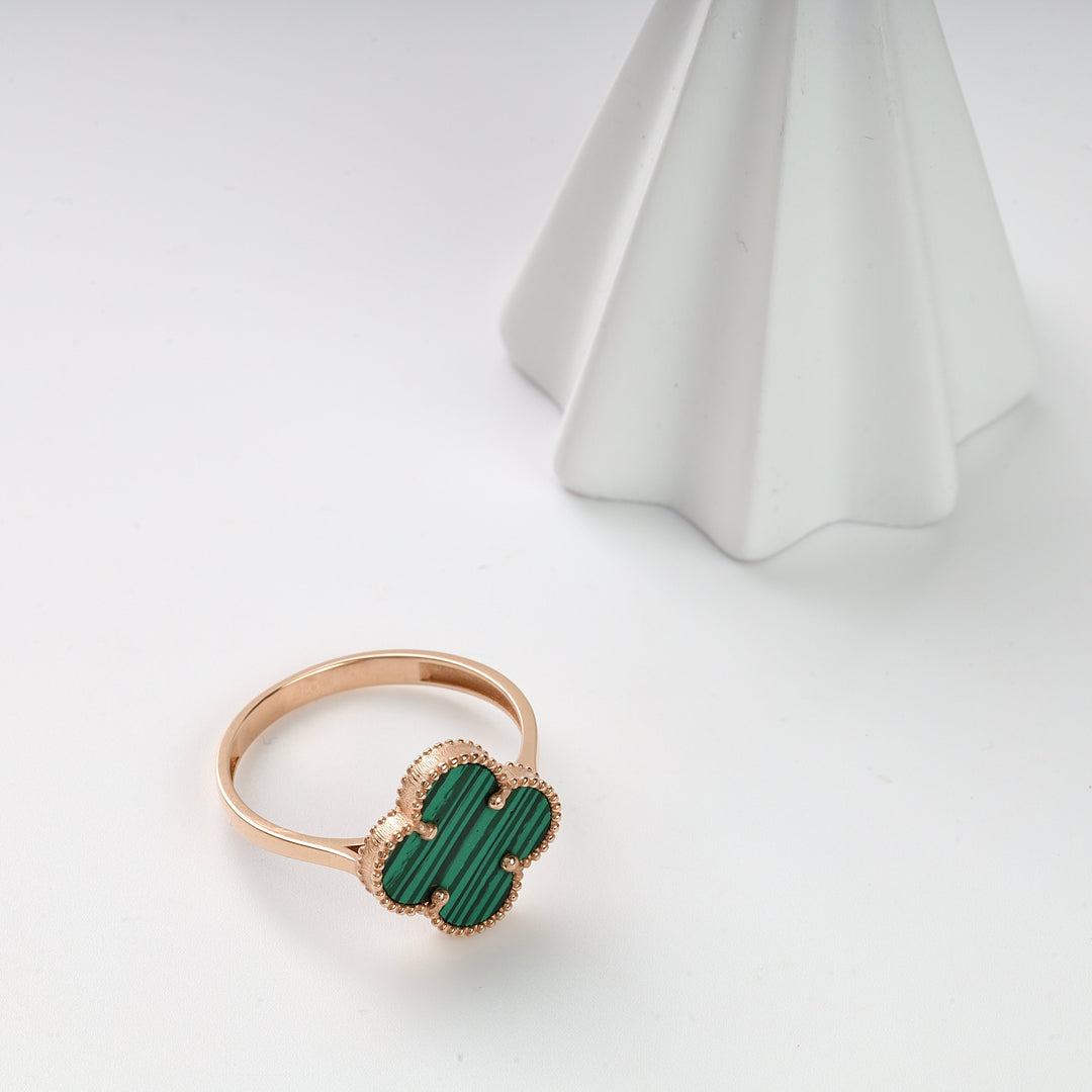 Gold ring with a green malachite clover-shaped motif displayed on a white surface with a geometric object.
