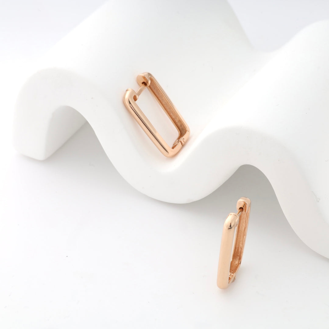 Rose gold rectangular hoop earrings on a white wavy surface.