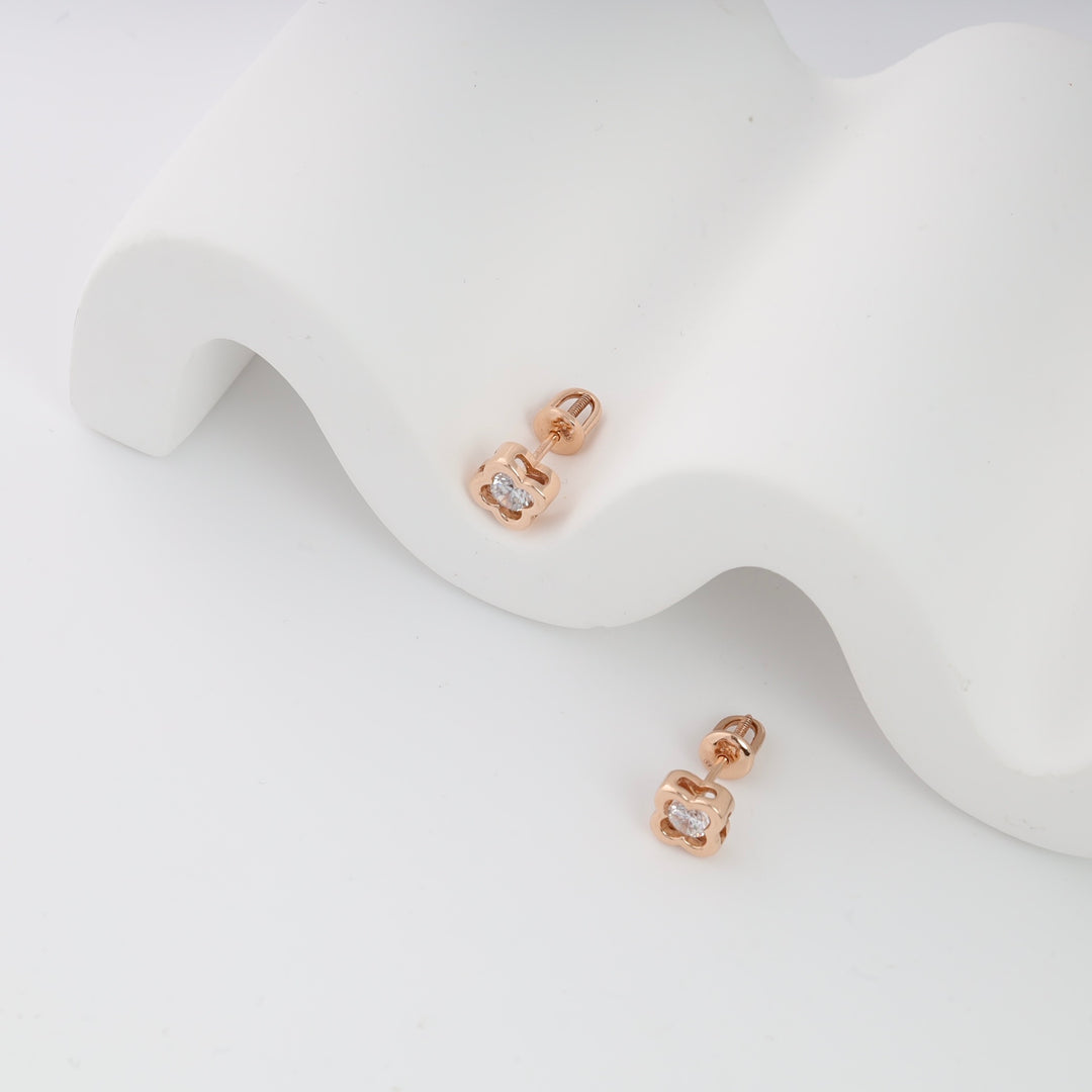 Rose gold stud earrings with clear stones on a white wavy surface.