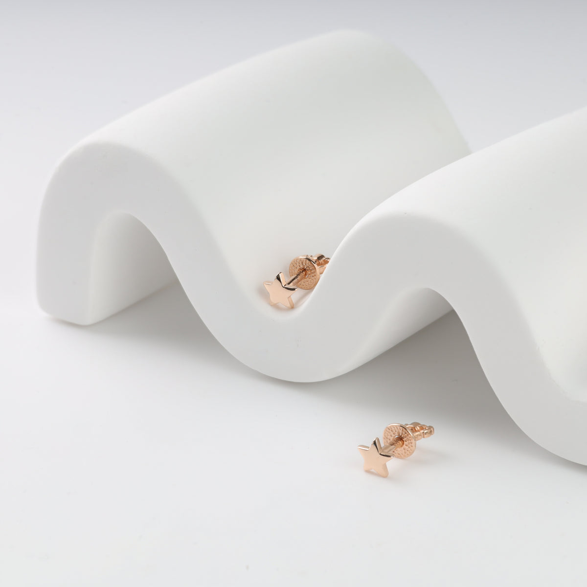 Rose gold star-shaped earrings on a wavy white surface.