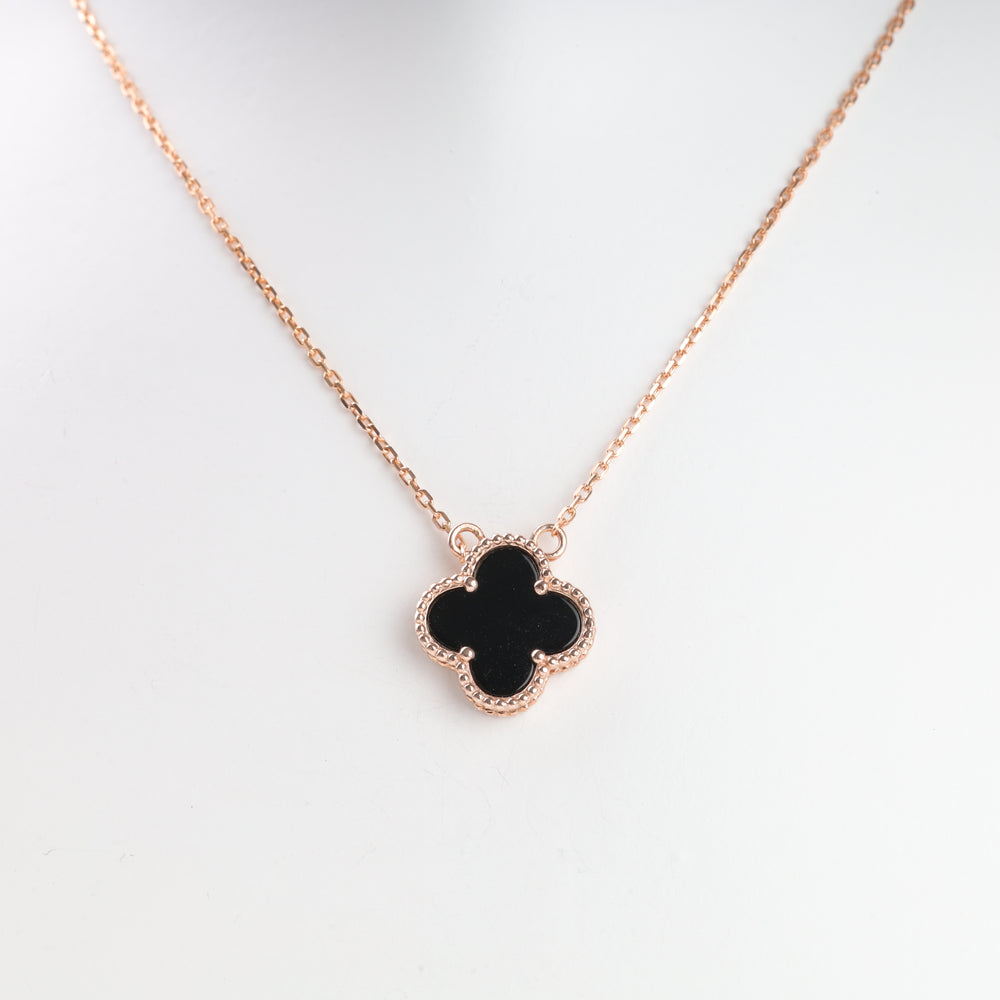 Gold chain necklace with a black clover pendant, displayed on a white background.