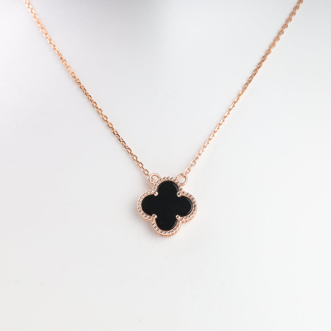 Gold chain necklace with a black clover pendant, displayed on a white background.
