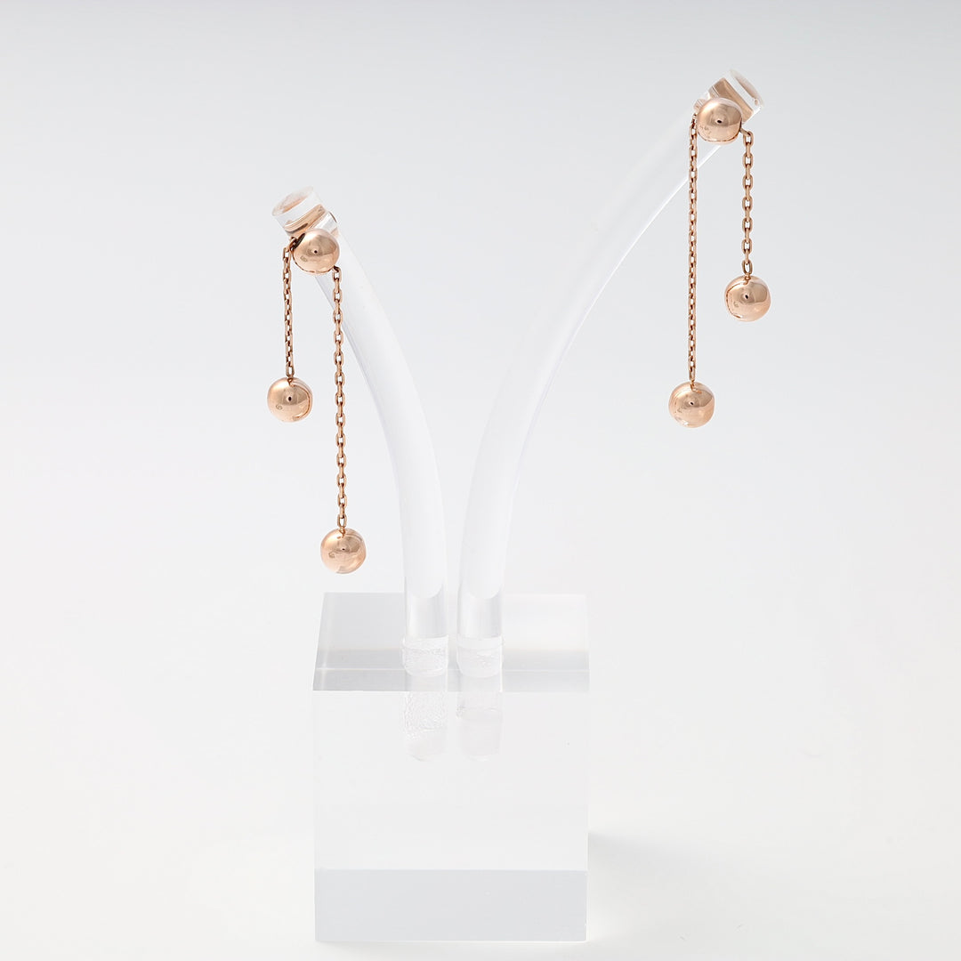 Pair of rose gold dangle earrings with two ball charms on each, displayed on a clear stand.