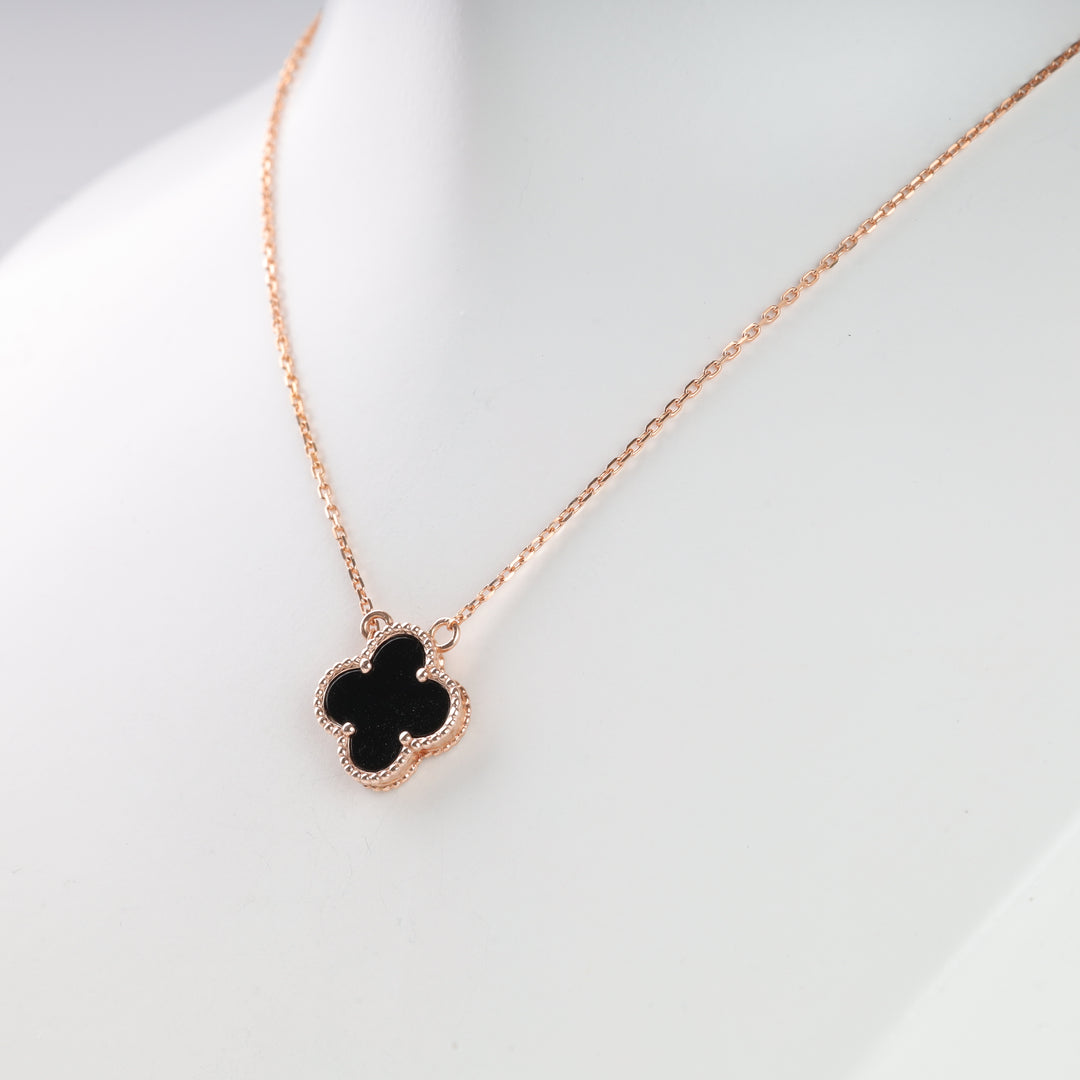 Gold chain necklace with a black enamel quatrefoil pendant, displayed on a white mannequin.