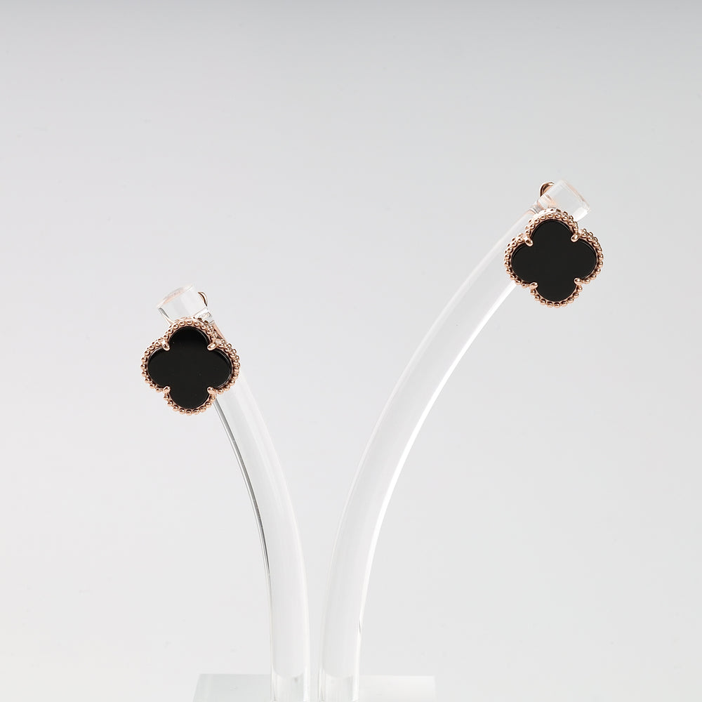 Pair of clover-shaped black enamel stud earrings with gold trim displayed on clear stands.