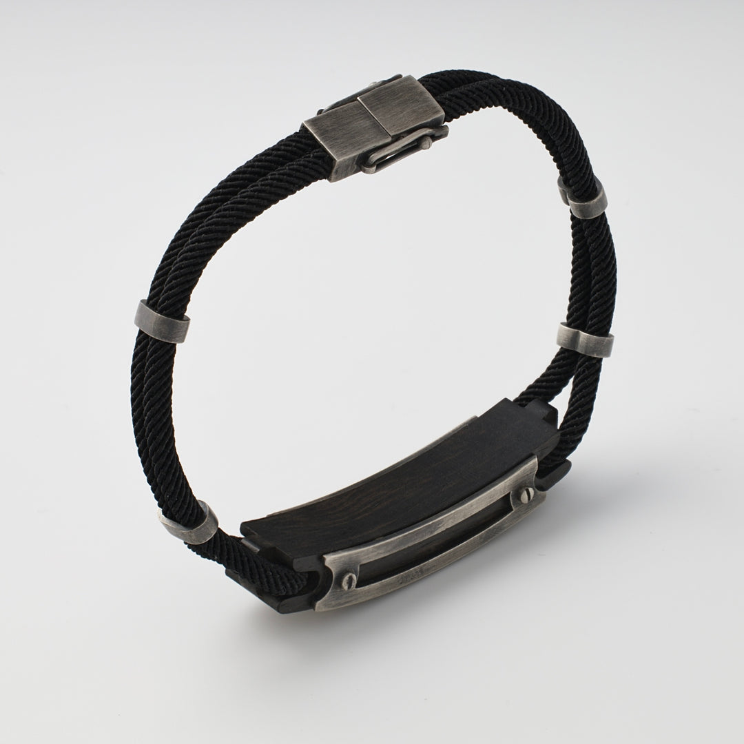 Black cord bracelet with silver metal accents and a rectangular metal plate, displayed on a white background.