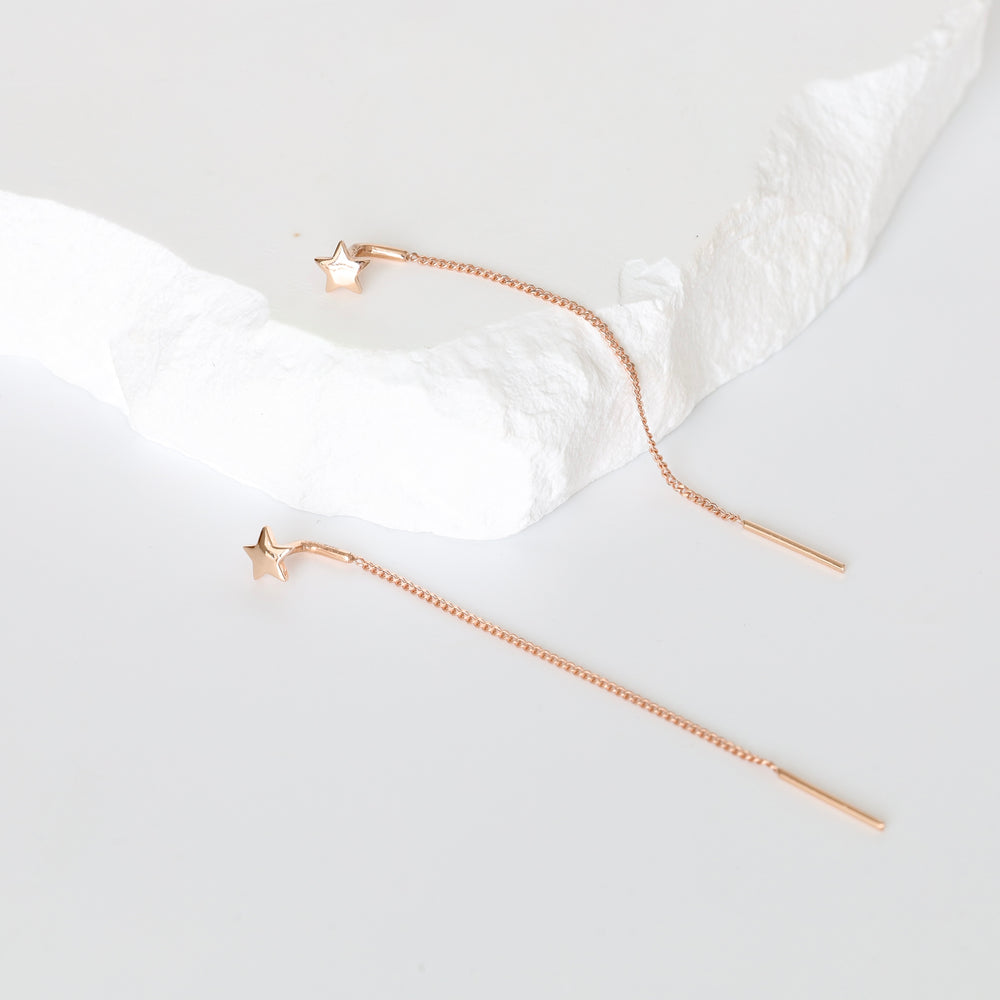 Pair of rose gold star threader earrings with long chains on a white textured slab, rose gold threader earrings, long chain earrings.