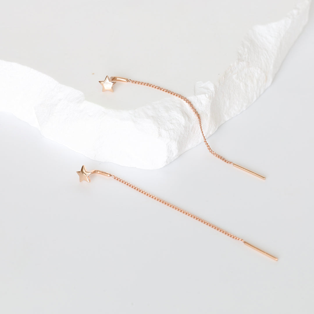 Pair of rose gold star threader earrings with long chains on a white textured slab, rose gold threader earrings, long chain earrings.