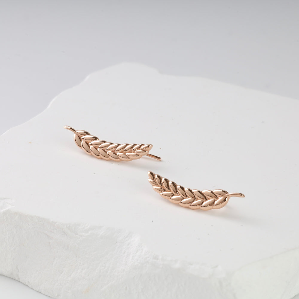 Pair of rose gold leaf motif ear climber earrings displayed on a white textured surface.