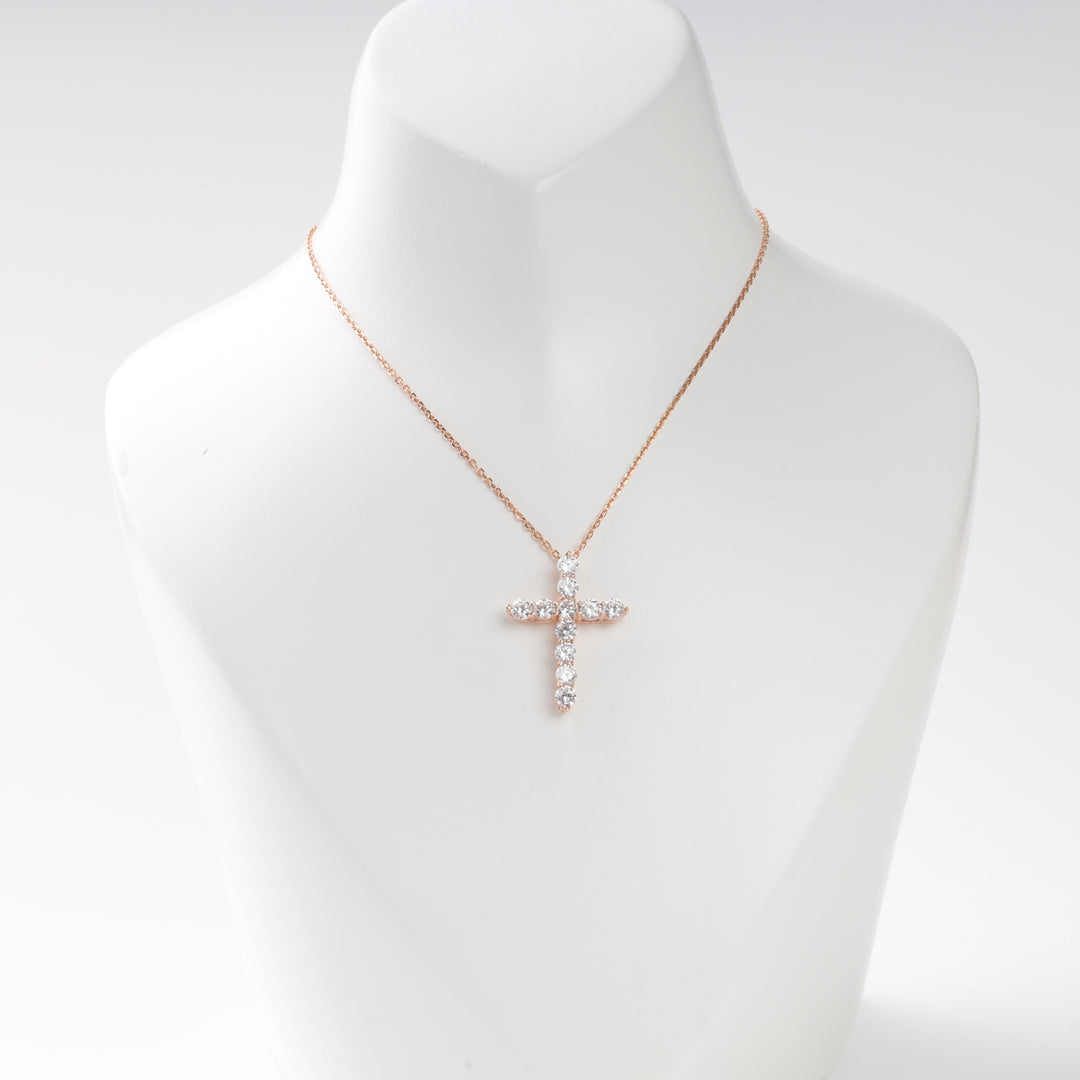 Rose gold necklace with a cross pendant made of clear round gemstones displayed on a white stand.