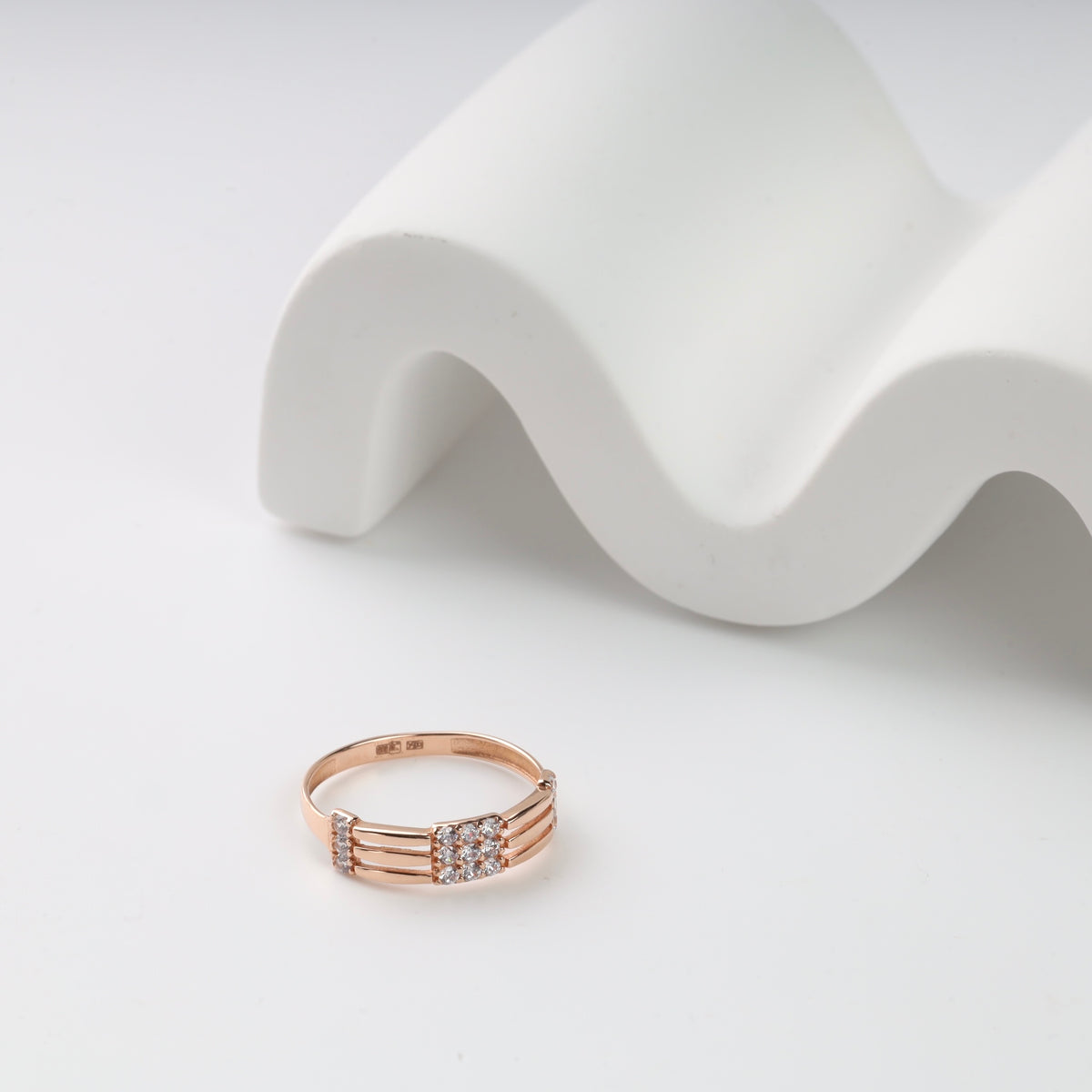 Rose gold ring with diamond accents on a white wavy surface.