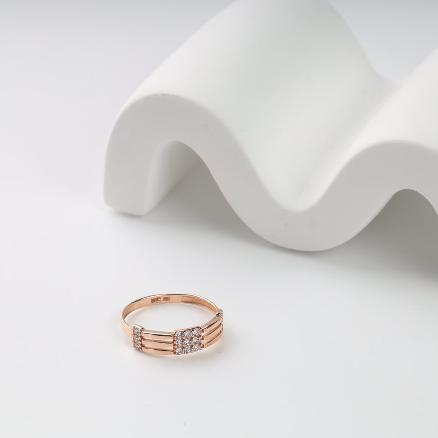 Rose gold ring with diamond accents on a white wavy surface.