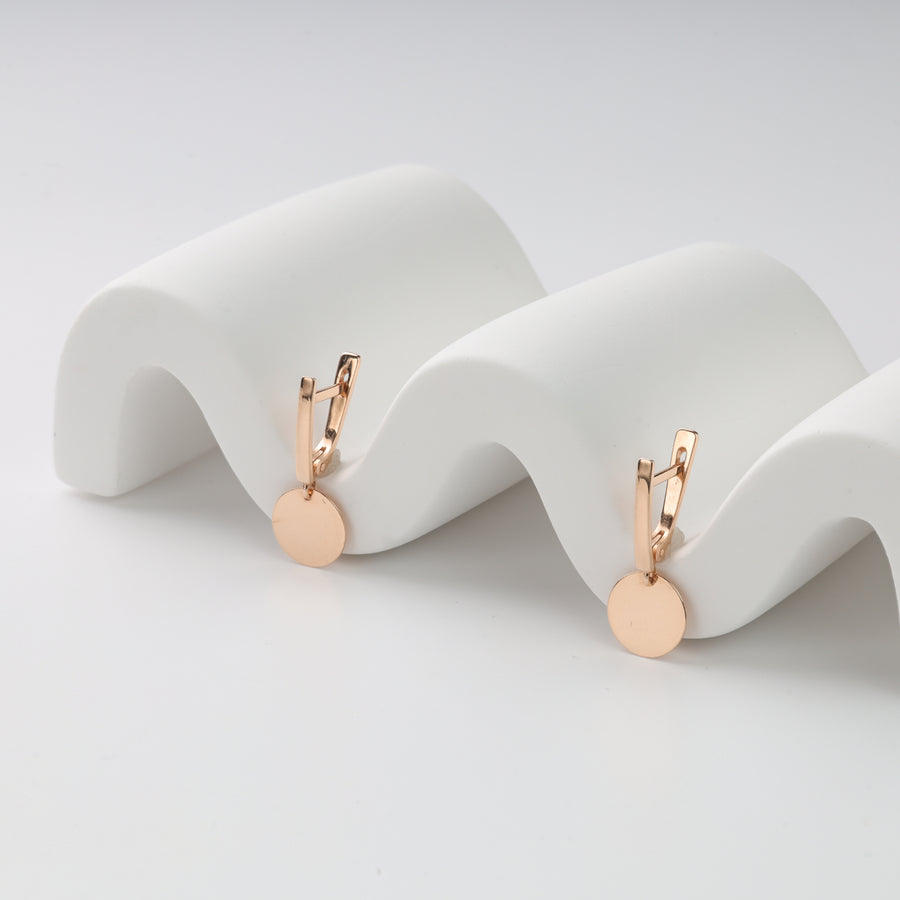 Rose gold disc dangle earrings displayed on white wave stand.