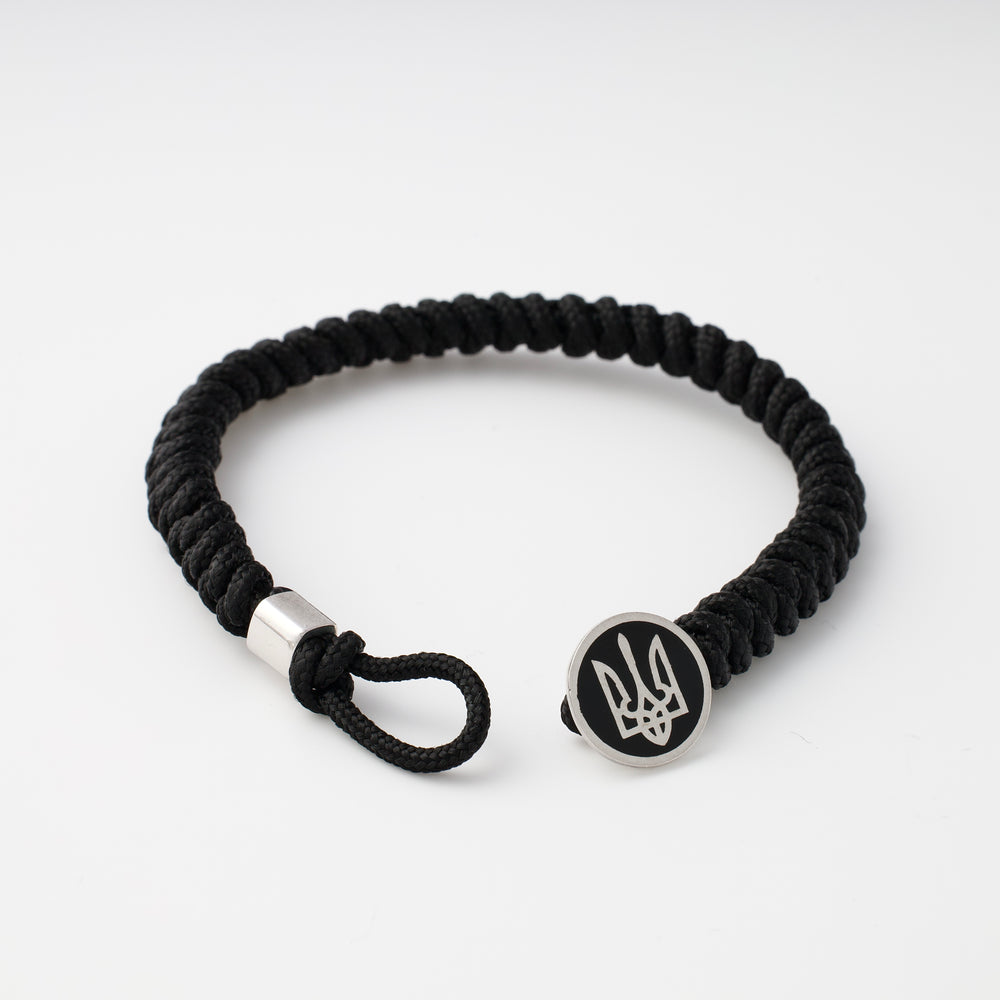 Black braided cord bracelet with a round metal charm engraved with a trident symbol, shown on a white background.