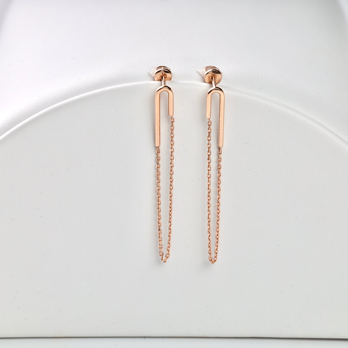 Rose gold chain earrings with vertical bar motifs displayed on a white stand.