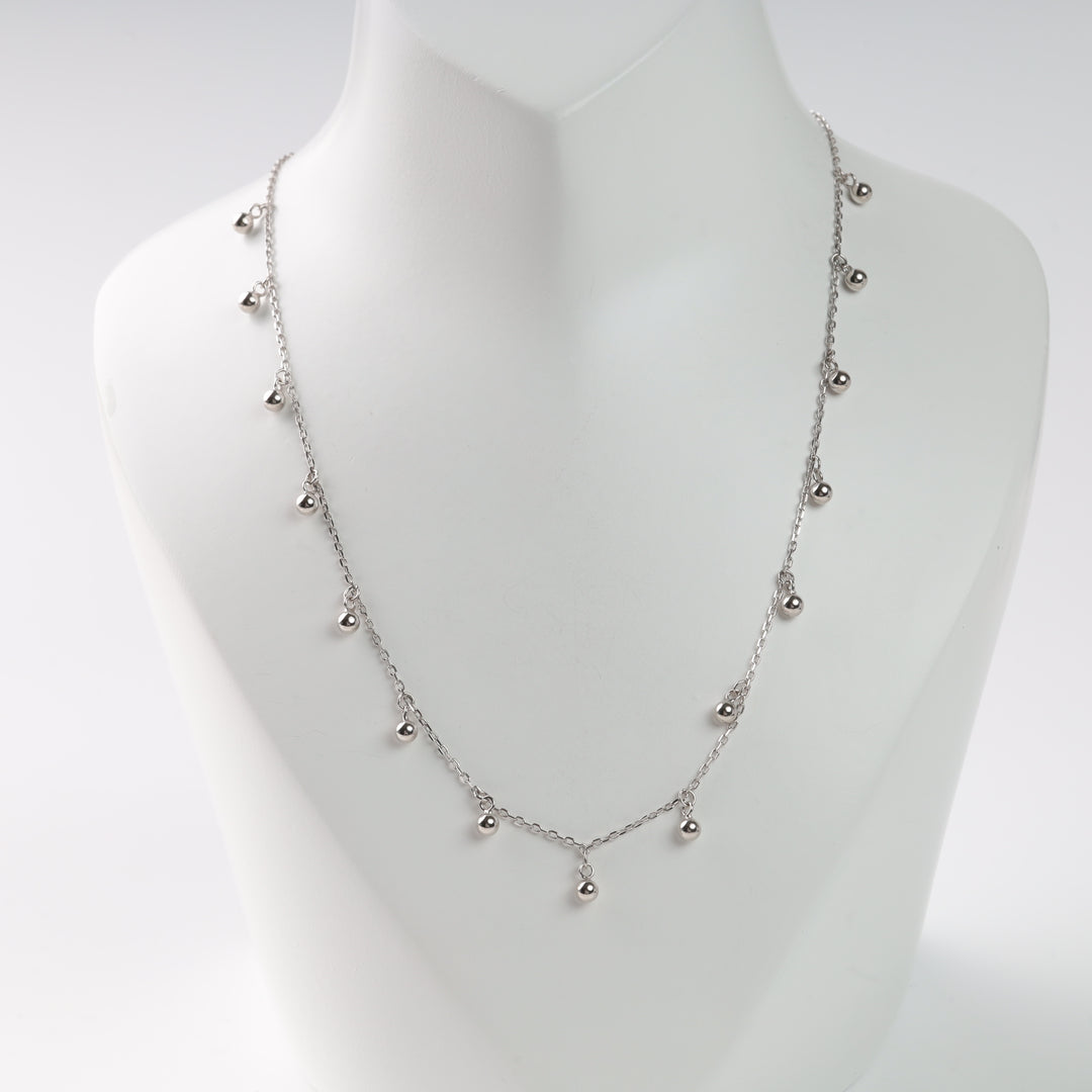 Silver ball charm necklace on a white display.