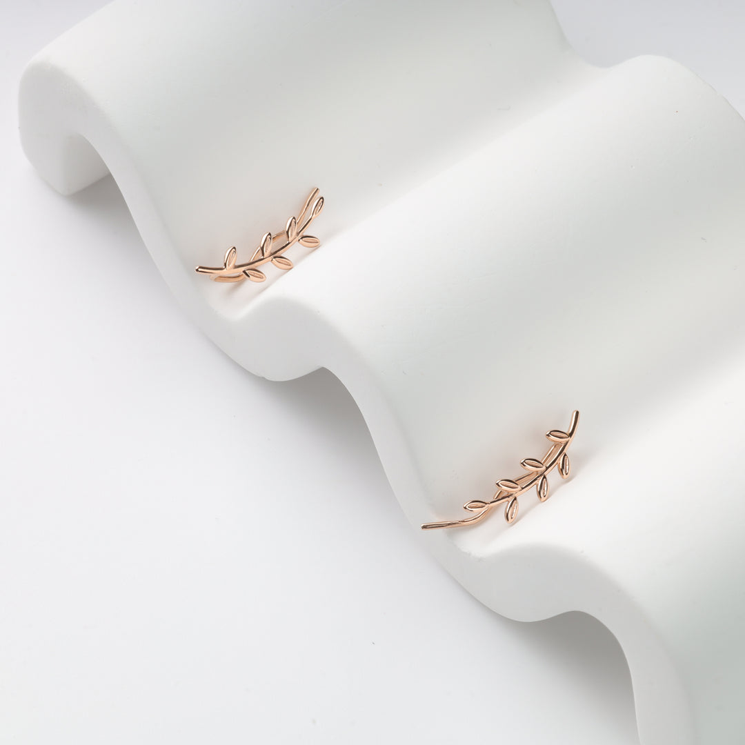 Pair of rose gold leaf ear climbers on white wavy display, metal branch earrings, ear crawler studs.