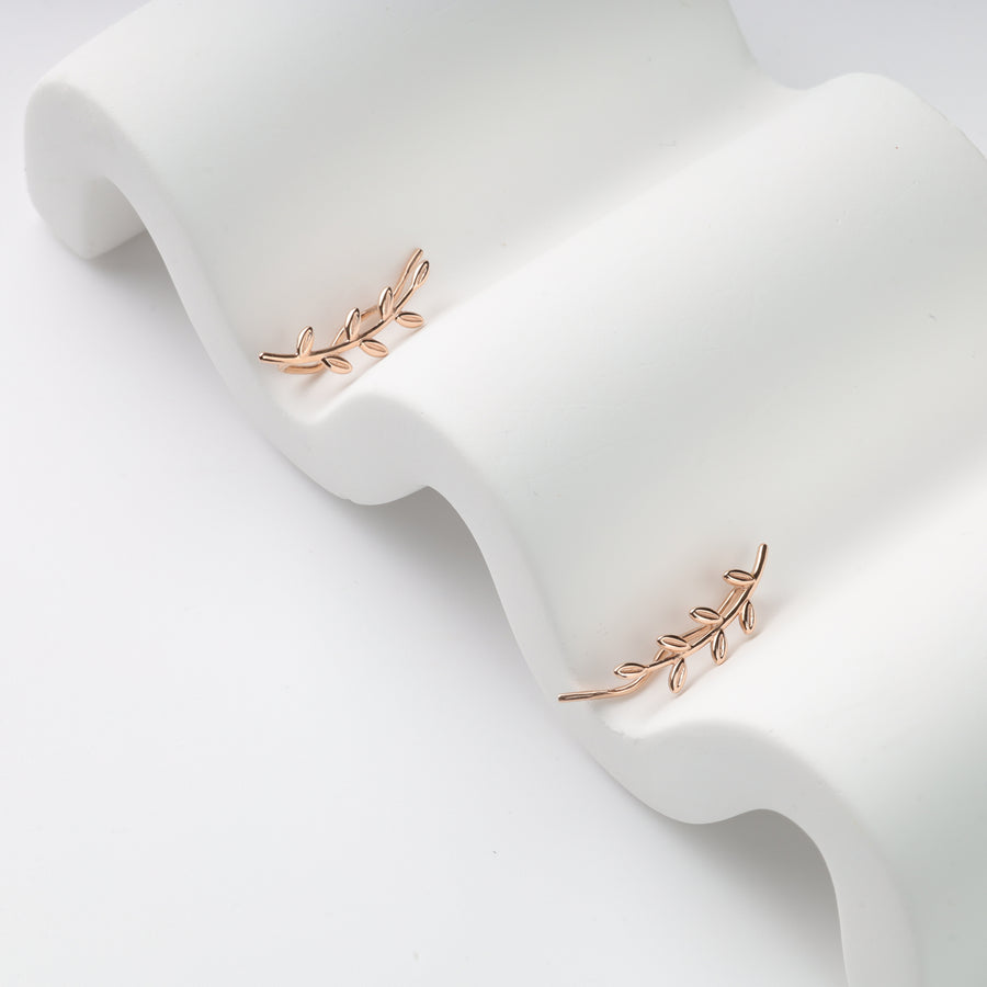 Pair of rose gold leaf ear climbers on white wavy display, metal branch earrings, ear crawler studs.