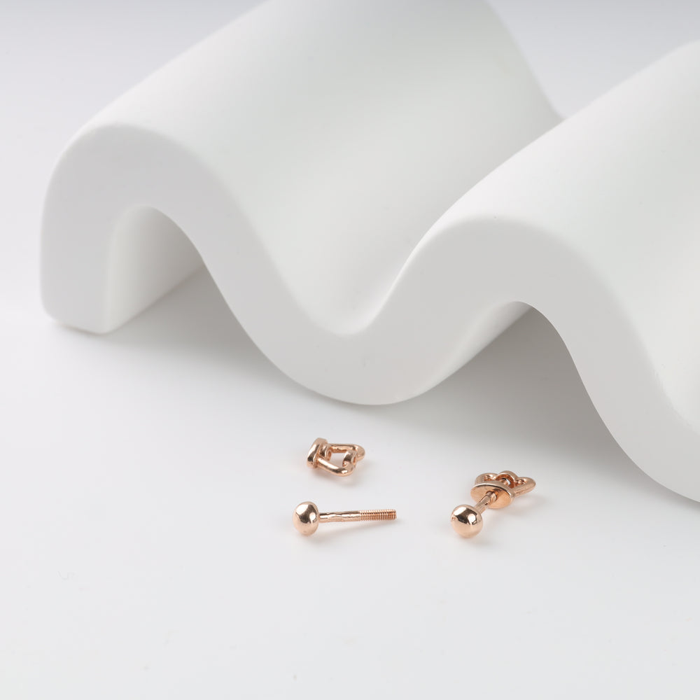 Rose gold ball stud earrings on a white wave surface.