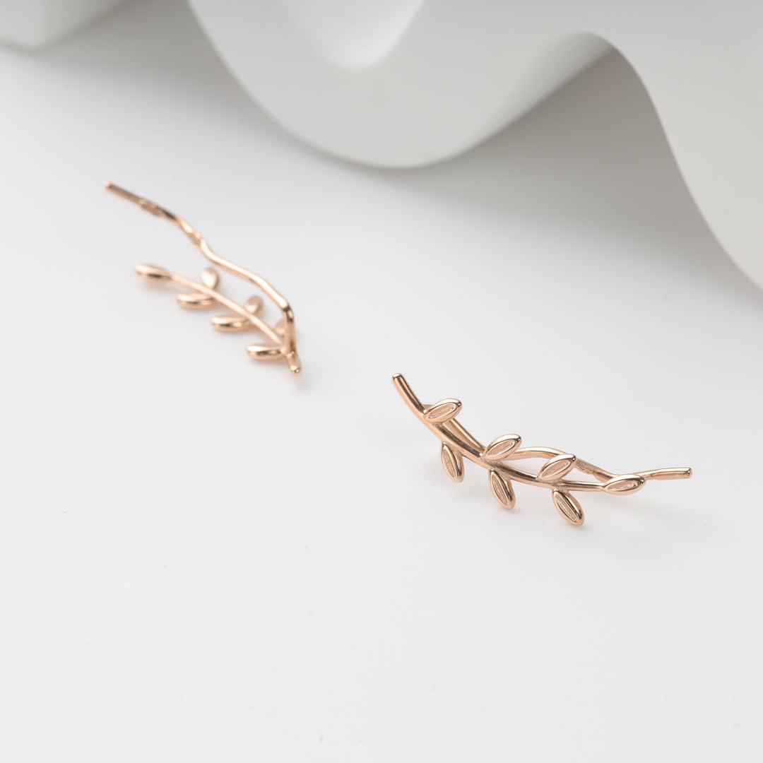 Pair of rose gold leaf branch ear climber earrings on white backdrop with folded paper, rose gold leaf earrings and ear climbers.