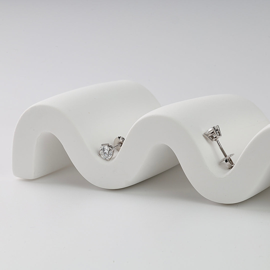 Pair of silver stud earrings with round clear gemstones displayed on a white wavy stand, minimalist jewelry.