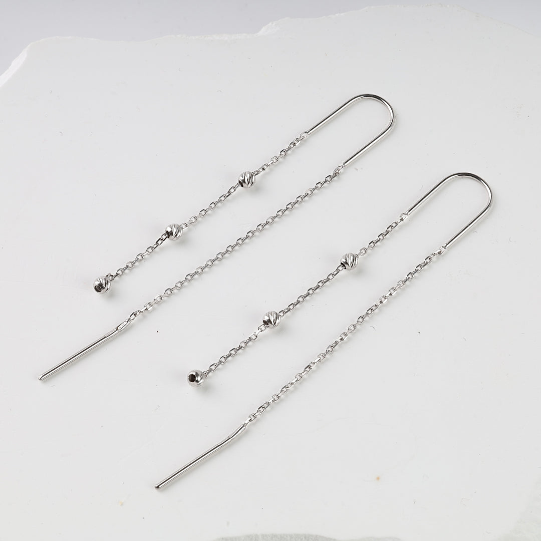 Pair of sterling silver threader earrings with delicate chains and small textured beads displayed on a white surface.