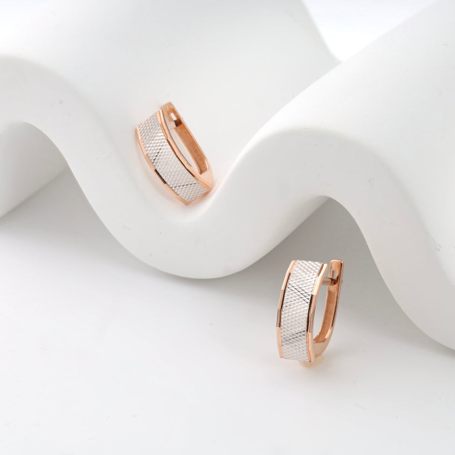 Rose gold and silver textured huggie earrings on a white wave background.