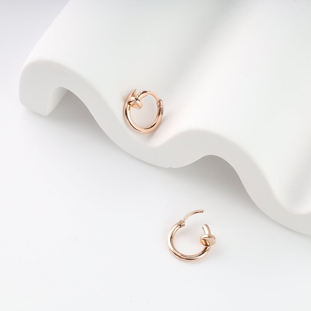 Pair of small rose gold hoop earrings with knot detail displayed on a white wavy surface.