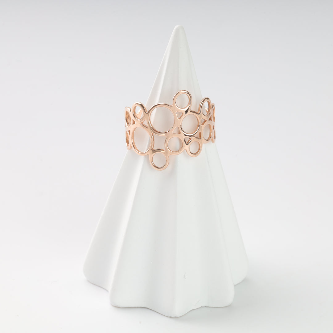 Rose gold openwork ring with a circles pattern, displayed on a white ceramic cone. Modern geometric jewelry.