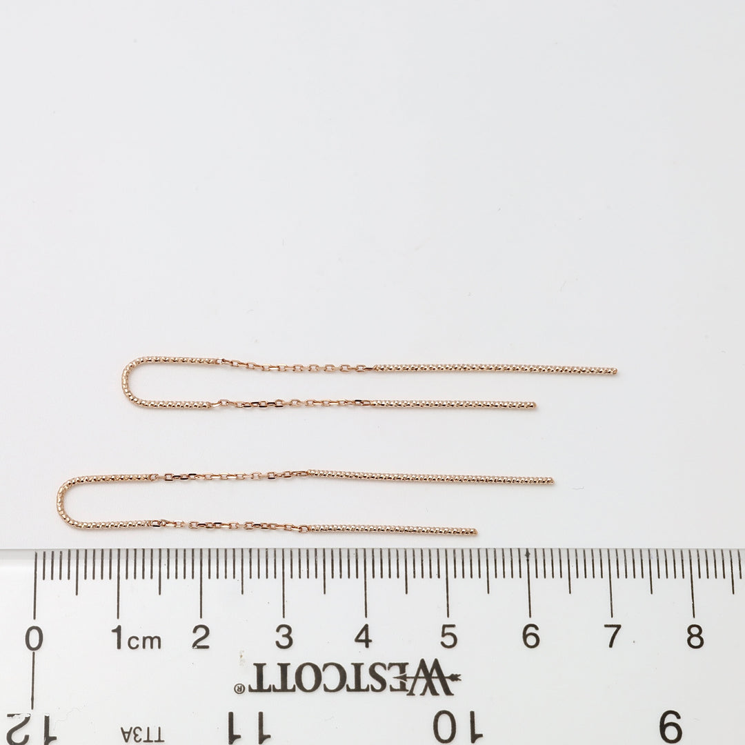 Pair of thin 14k gold threader chain earrings laid by a ruler on white background, minimalist Ukrainian Jewelry for women.