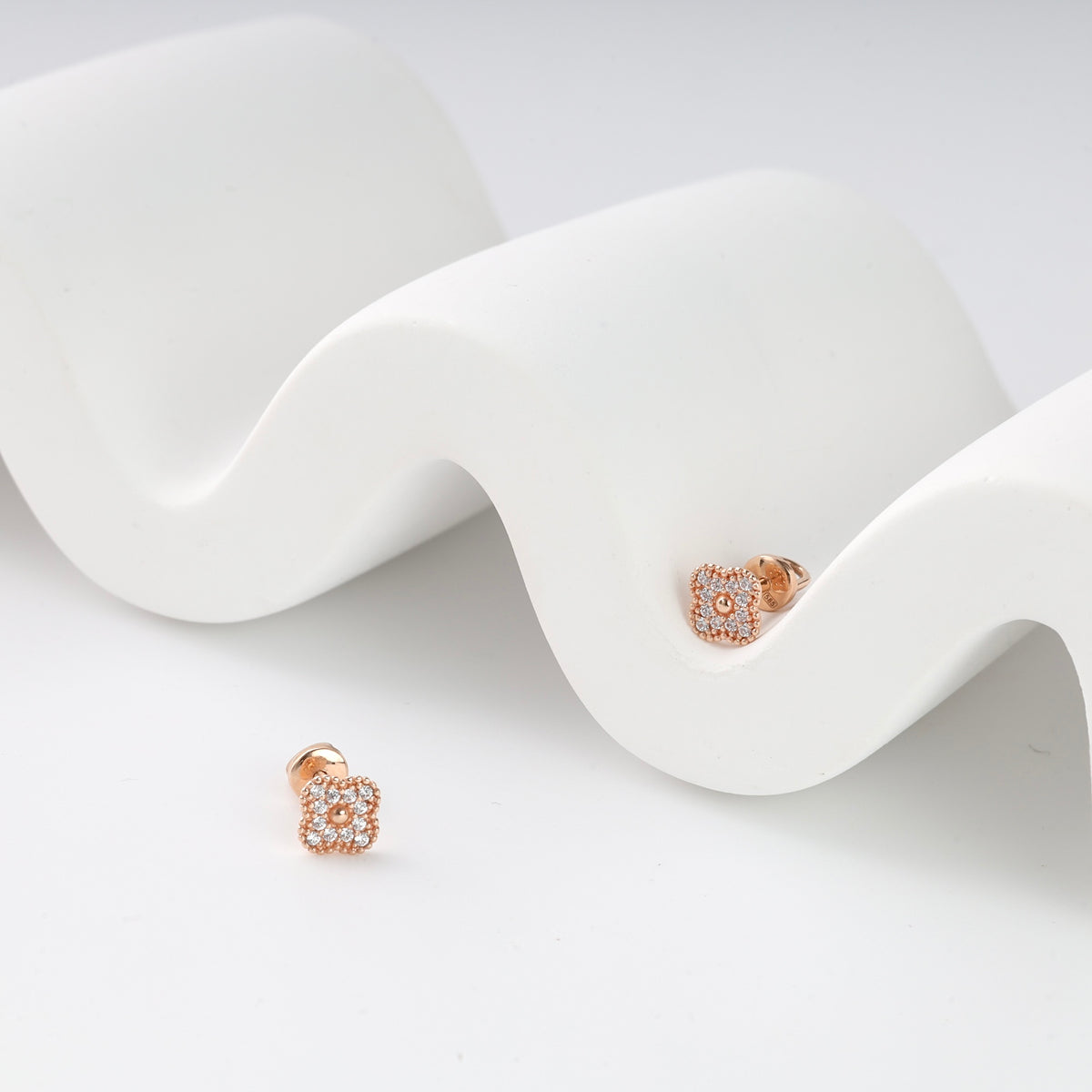 Rose gold square stud earrings with clear crystals displayed on a white wavy background.