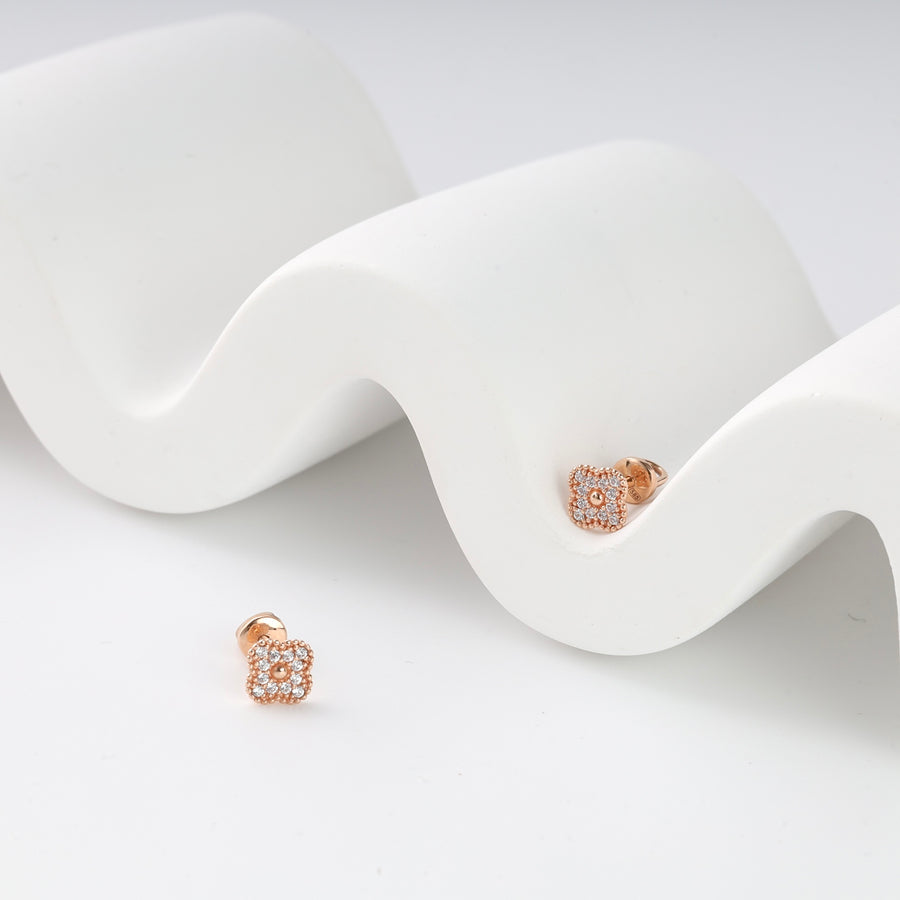 Rose gold square stud earrings with clear crystals displayed on a white wavy background.
