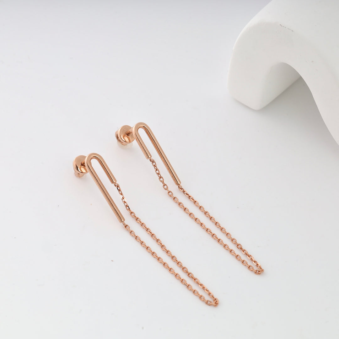 Rose gold chain drop earrings on a white surface.