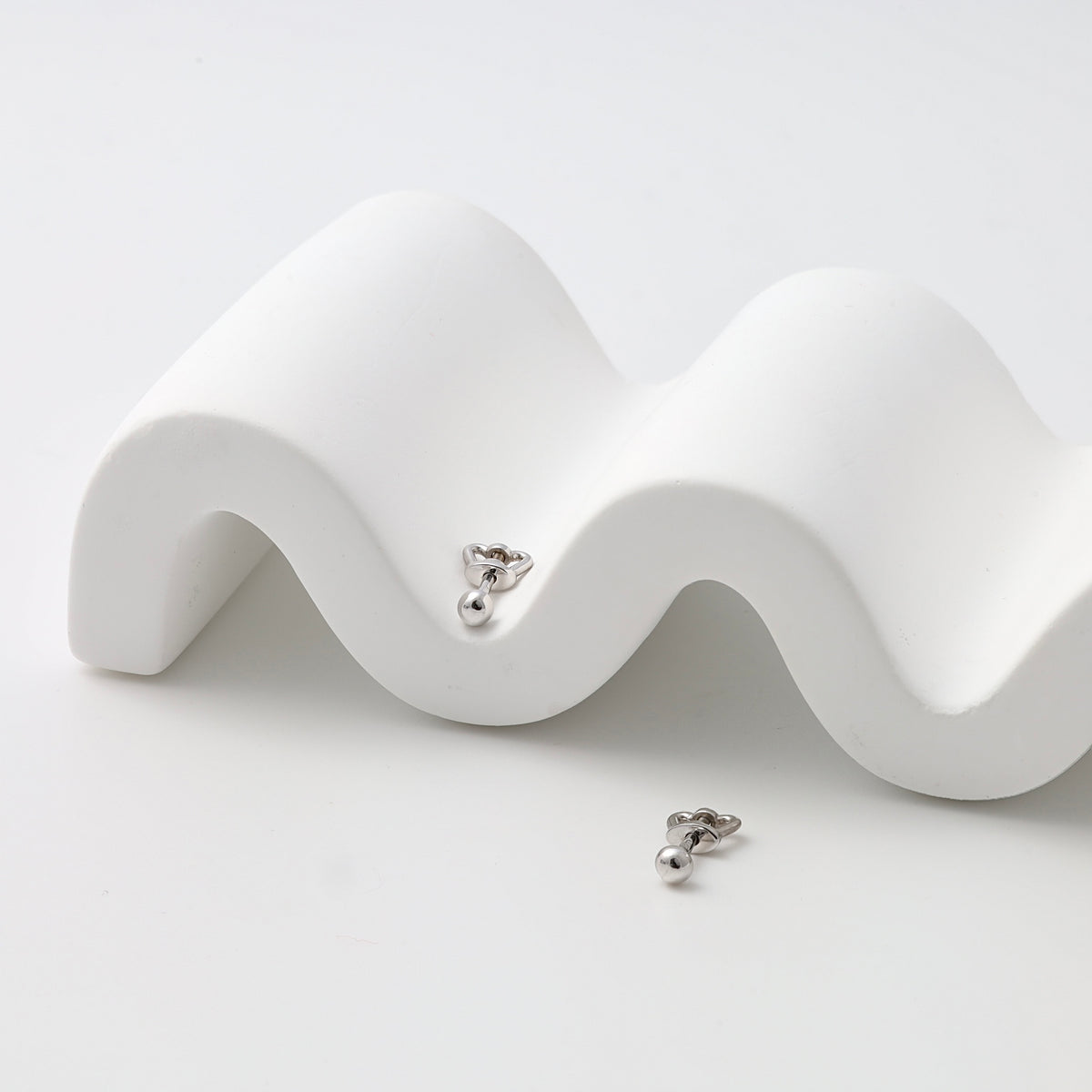 Pair of sterling silver heart stud earrings with drop ball detail on white display, minimalist Ukrainian Jewelry for everyday studs.