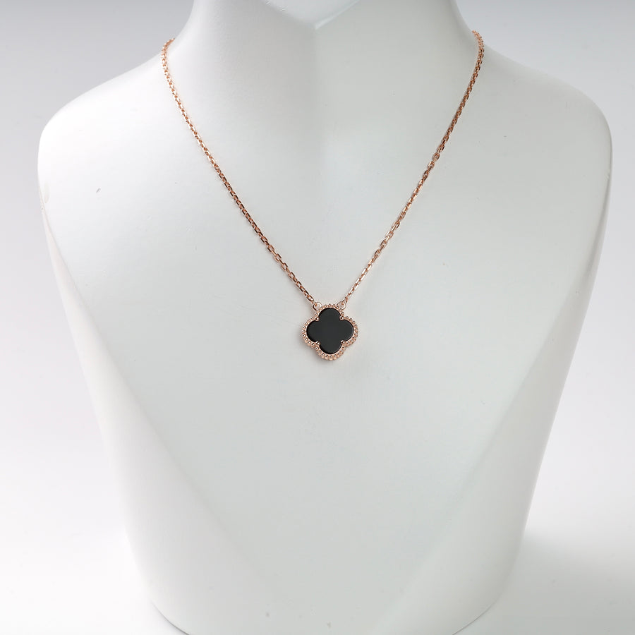 Gold chain necklace with a black clover-shaped pendant displayed on a white bust.