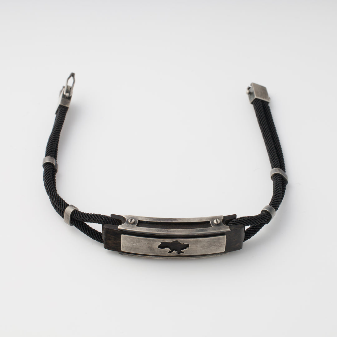Black cord bracelet with a silver metal plate featuring a cutout map motif, displayed on a white background.