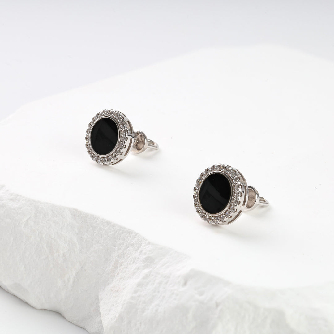 Pair of silver stud earrings with black oval stones and clear crystal halo displayed on a white stone surface.