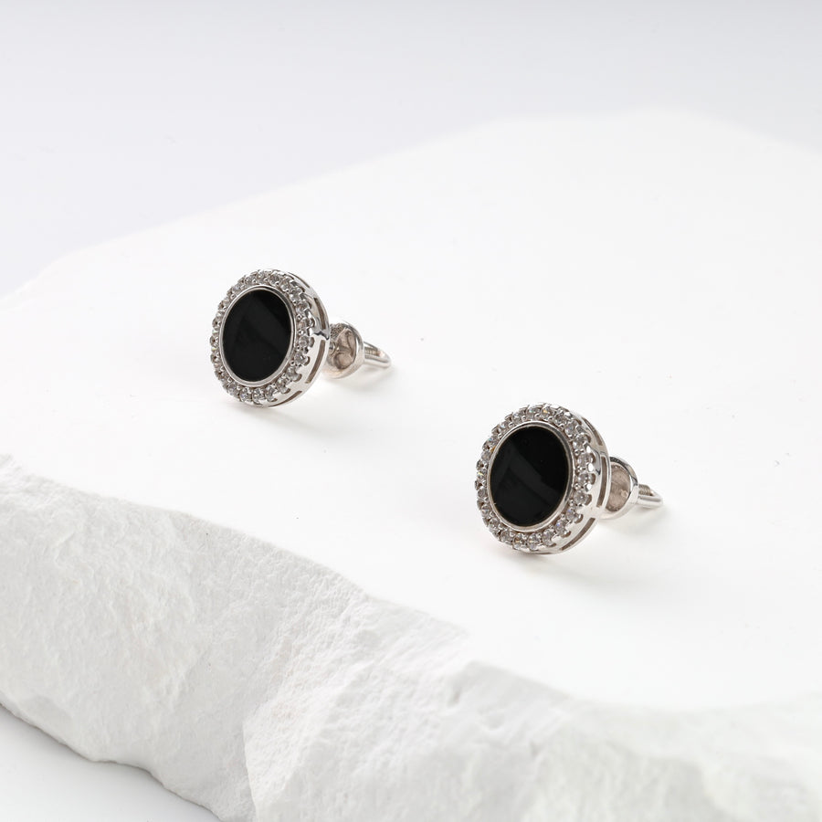 Pair of silver stud earrings with black oval stones and clear crystal halo displayed on a white stone surface.