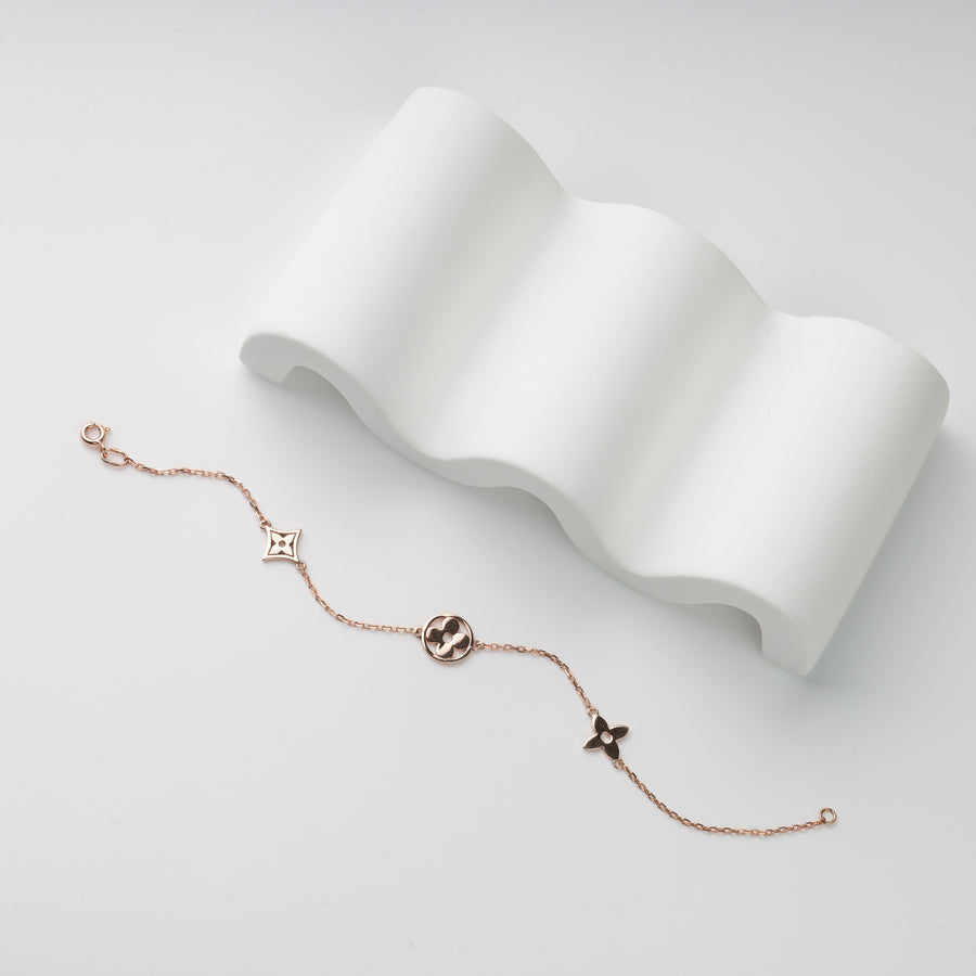 Single rose gold chain bracelet with three flower charms, including clover motifs, displayed on a white wavy prop.