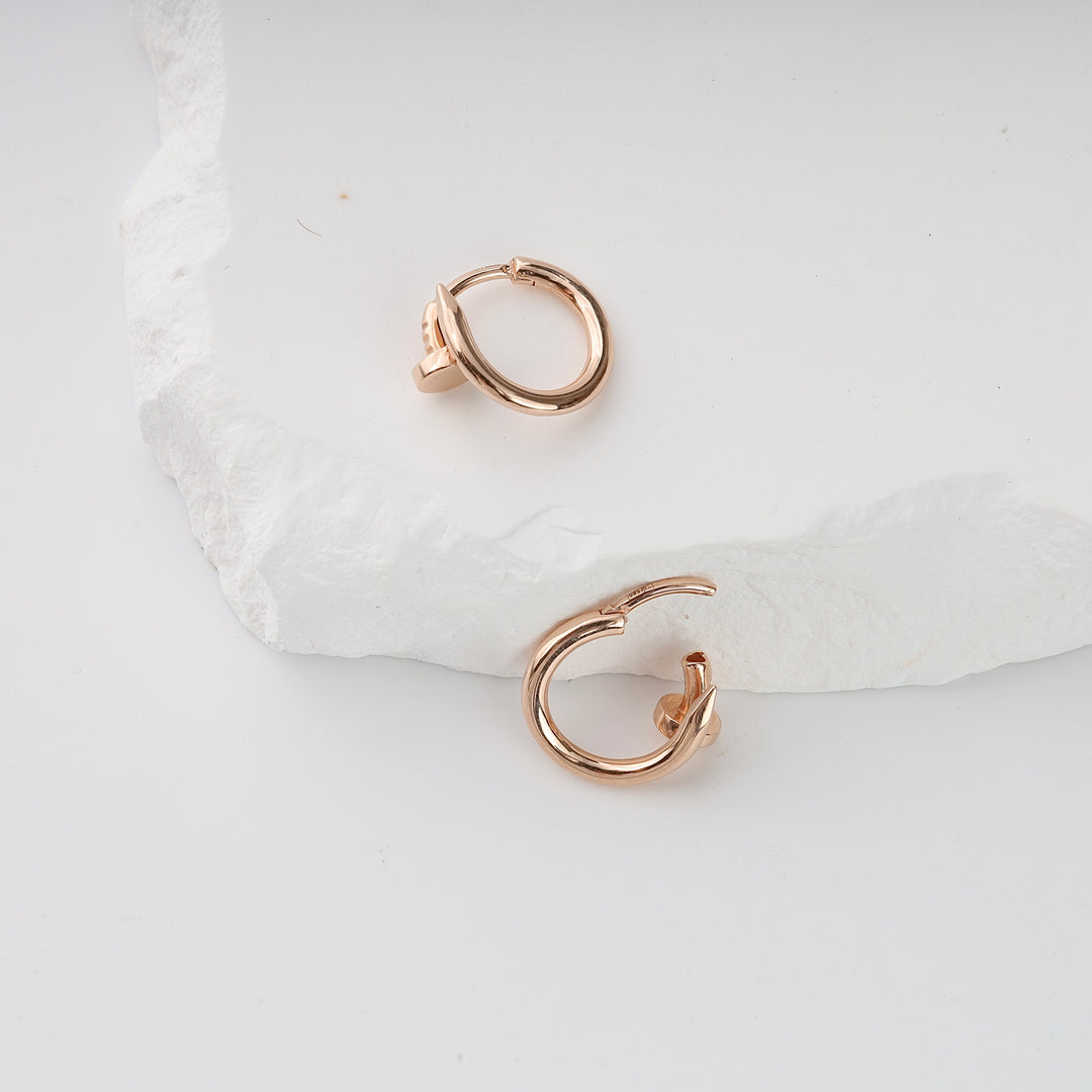 Pair of rose gold twisted hoop earrings displayed on a white textured surface, minimalist jewelry style.