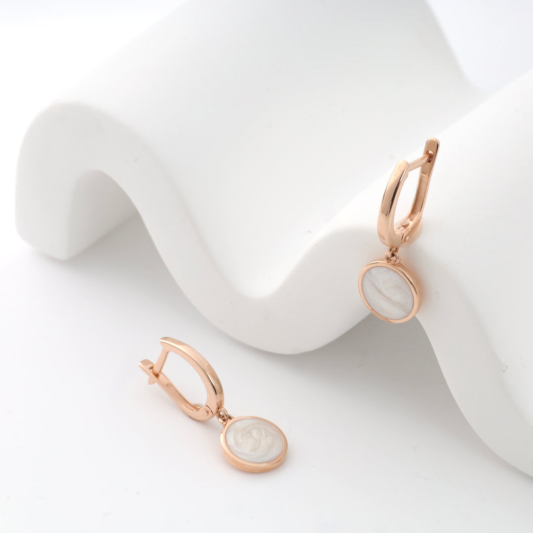 Rose gold earrings with circular white pearl pendants on a white wave-pattern display.