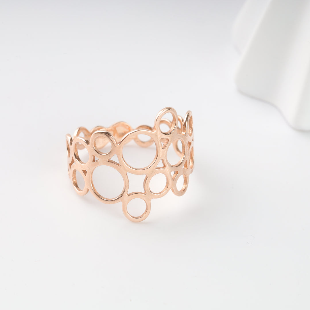Openwork rose gold ring with circle and square cutout pattern on a white background, modern statement jewelry.