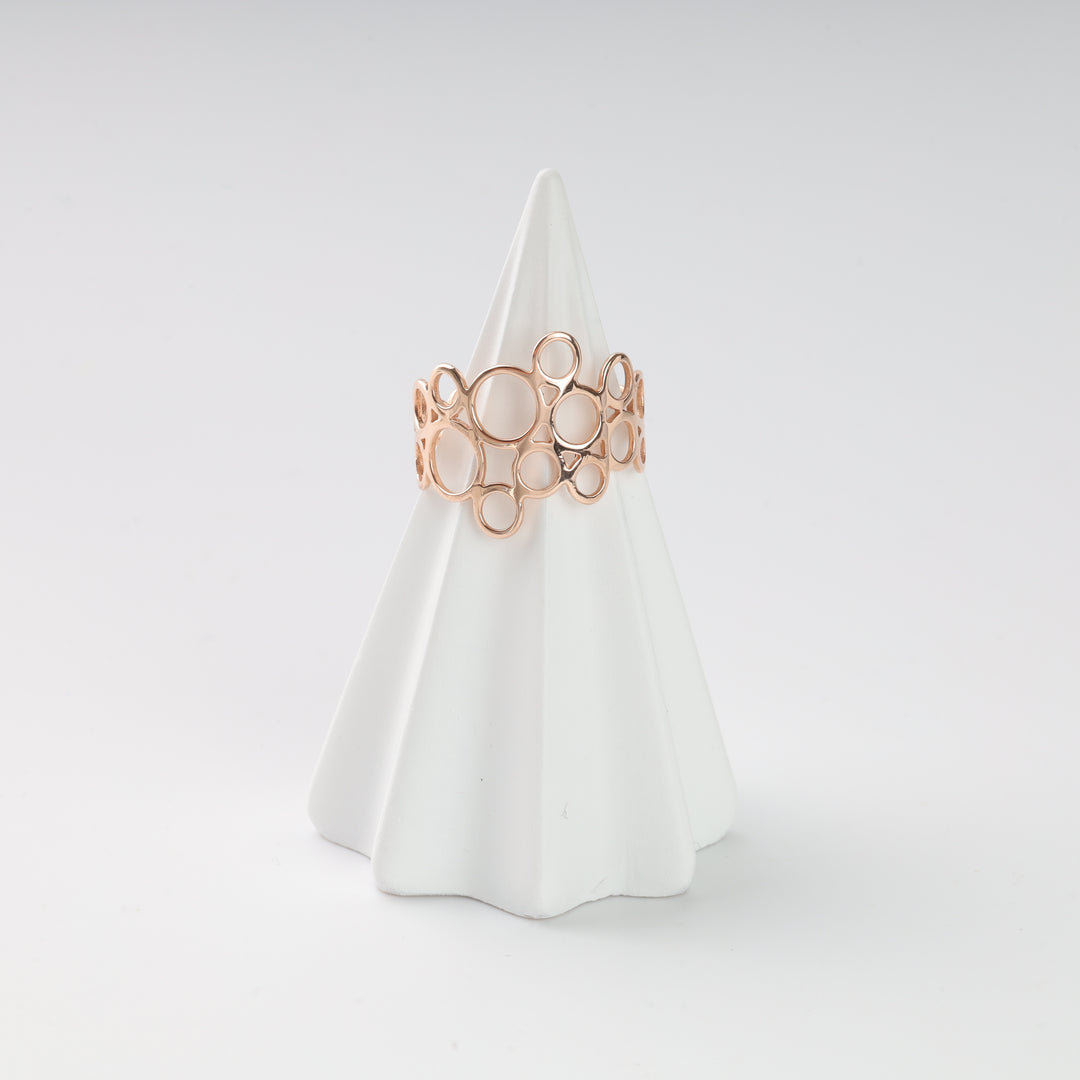 Rose gold bubble circle band ring with openwork design, displayed on a white ceramic ring holder.