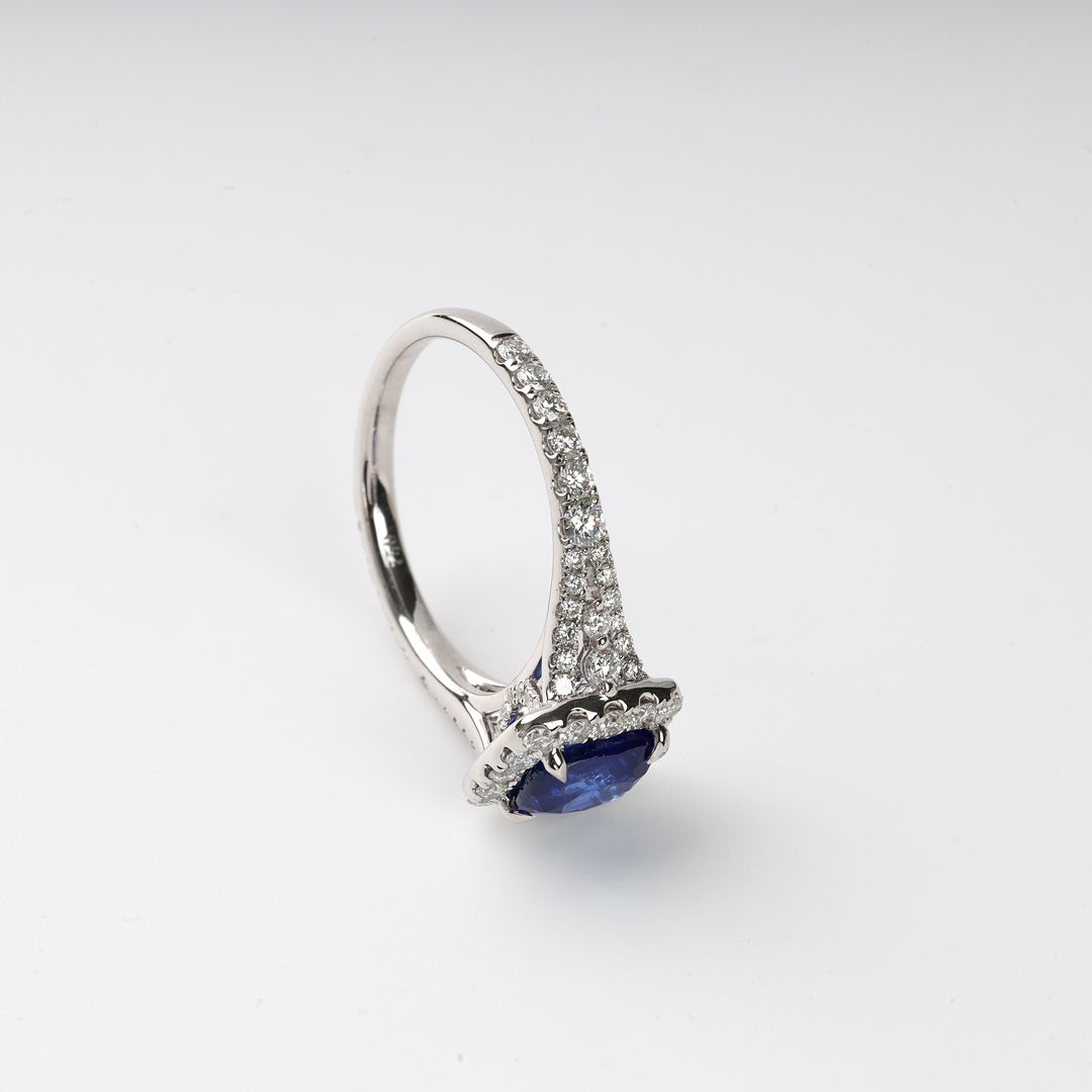 White gold ring with a blue oval gemstone and pavé diamonds set on the band, displayed on a white background.